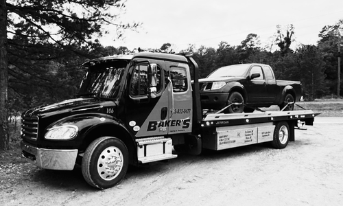 Flatbed tow truck transporting a Nissan Frontier pickup on gravel driveway