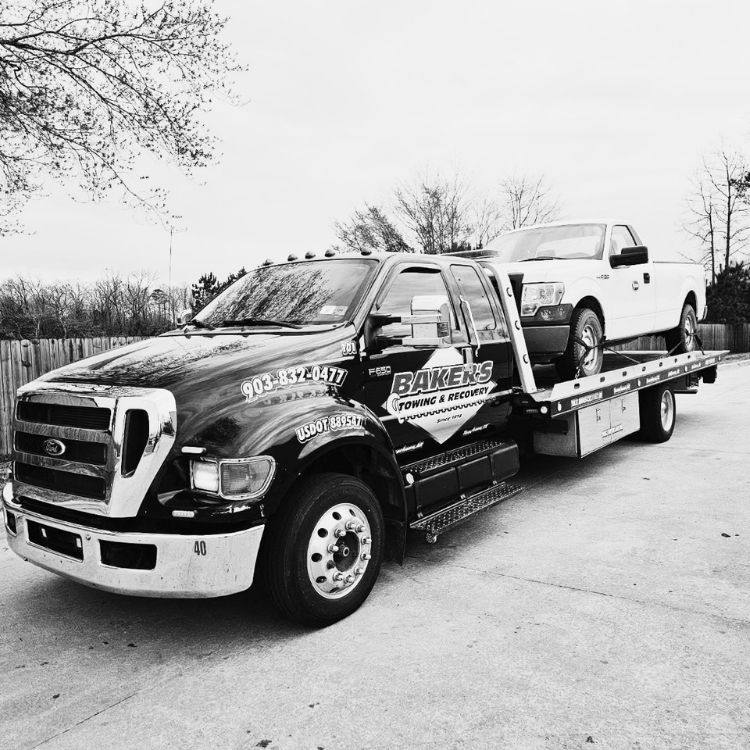 Flatbed tow truck transporting a white Ford F-150 work truck on concrete lot