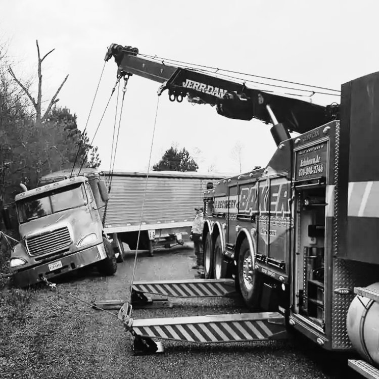 Heavy-duty Baker towing truck using crane to recover a stuck semi-truck in wooded area